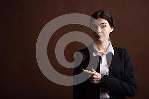 Portrait of serious brunette business woman pointing her finger to the side in studio on brown background with copyspace.