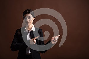 Portrait of serious brunette business woman pointing her finger to the side in studio on brown background with copyspace.