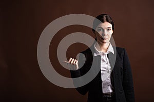 Portrait of serious brunette business woman pointing her thumb to the side in studio on brown background with copyspace.