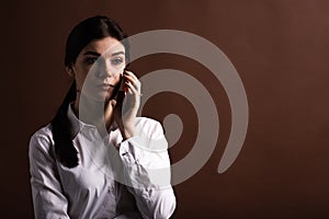 Portrait of serious brunette business woman talking on the phone in studio on brown background with copyspace.