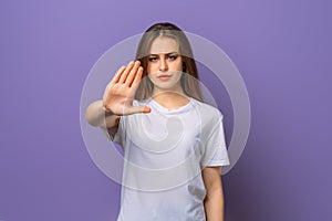 Portrait of serious brunette girl showing stop taboo sign, extending hand palm to prevent something, prohibit action, purple