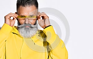 Portrait of serious brutal bearded middle aged man in yellow hoodie standing and putting on glasses