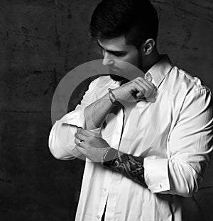 Portrait of serious brutal handsome bearded man with tattoo on hand buttin up sleeve of shirt