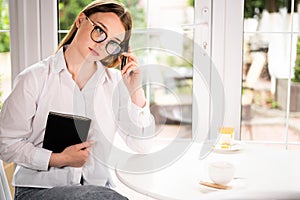 portrait of a serious business lady in a cafe sitting in glasses with a notepad talking on a mobile phone. Negotiations