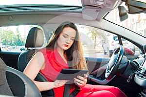 Portrait of serious business lady, caucasian young woman driver in red summer suit setting up the route on a navigator while