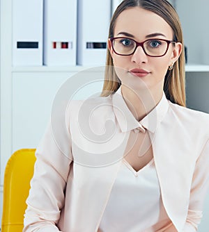 Portrait of young serious businesswoman looking at the camera while using laptop in office.