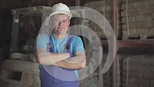 Portrait of serious Caucasian man in blue uniform and white helmet posing at factory or plant. Confident male employee