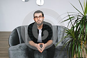 Portrait of serious caucasian man sitting on a sofa and looking on camera