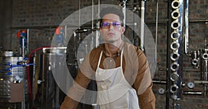 Portrait of serious Caucasian man working at gin distillery, using equipment and looking to camera