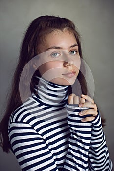 portrait of a serious Caucasian teenage girl in a striped jacket against a gray wall in the studio light from the window