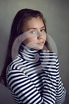 portrait of a serious Caucasian teenage girl in a striped jacket against a gray wall in the studio light from the window