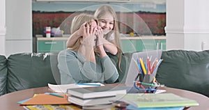 Portrait of serious Caucasian woman working with laptop as her joyful daughter coming up from the background and closing