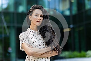 Portrait of serious confident hispanic woman outside office building, businesswoman looking thoughtfully at camera with