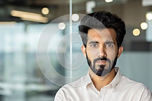 Portrait of a serious and confident Indian man standing in a shirt in the office and looking at the camera. A close-up