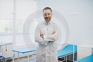 Portrait of a serious confident male doctor standing with arms crossed at medical office
