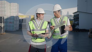 Portrait of serious confident Middle Eastern and Caucasian engineers walking in sunlight outdoors at warehouse talking