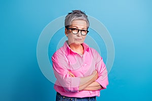 Portrait of serious confident person with grey hair wear stylish blouse in eyewear hold arms crossed isolated on blue