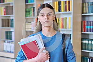 Portrait of serious confident student guy with textbooks looking at camera in college library