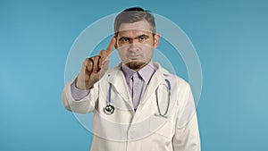 Portrait of serious doctor in professional medical white coat showing rejecting gesture disapproving with no finger sign