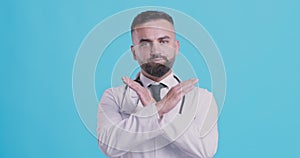 Portrait of serious doctor showing no, crossing hands as stop sign, negation gesture, blue studio background.