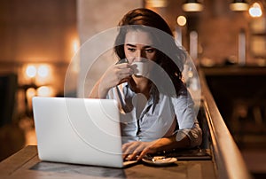 Portrait of serious elegant businesswoman sitting at modern restaurant working on her laptop and drinking coffee