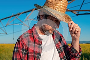 Portrait of serious farmer standing in front of center-pivot irrigation equipment in rapeseed field