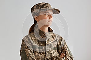 Portrait of serious female against light background indoor, looking away with pensive and serious facial expression, keeps arms