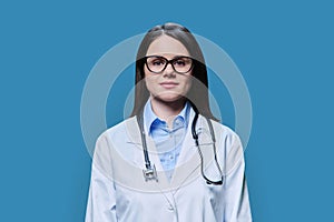 Portrait of serious female doctor looking at camera on blue background