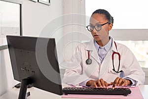 Portrait of serious female doctor looking at monitor and typing