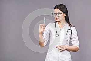 Portrait of serious female doctor in medical mask holding syringe for injection isolated on grey background