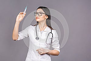 Portrait of serious female doctor in medical mask holding syringe for injection isolated on grey background