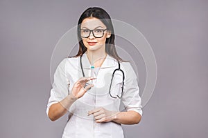 Portrait of serious female doctor in medical mask holding syringe for injection isolated on grey background