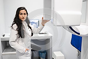 Portrait of serious female medic with arm crossed in CT scan room. Woman near the dental tomograph.