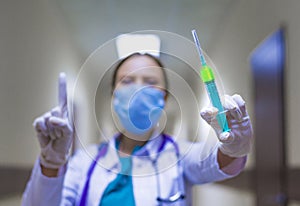 Portrait of serious female medical doctor or nurse with stethoscope in the hospital corridor and showing attention sign.