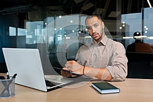 Portrait of serious and focused businessman, man looking thinking at camera writing and signing document inside office