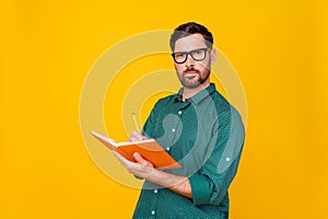 Portrait of serious gloomy man wear stylish shirt in glasses write in copybook on lecture in college isolated on yellow