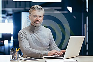 Portrait of serious gray haired boss, man looking at camera thinking, mature businessman inside office working at desk