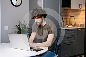 Portrait of serious handsome bearded young business man working on project at laptop typing, using online app sitting at