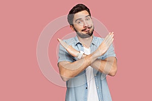 Portrait of serious handsome bearded young man in blue casual style shirt standing with X sign hands and looking at camera