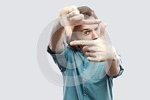 Portrait of serious handsome long haired blonde young man in blue casual shirt standing with cropping composition gesture. focus