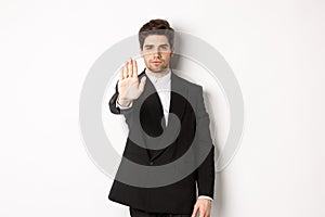 Portrait of serious handsome man in formal suit, extending hand to stop you, prohibit action, forbid and disagree with