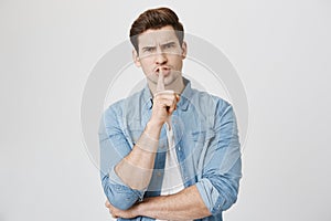 Portrait of serious handsome man, looking worried, showing shh gesture with index finger near mouth, isolated over white