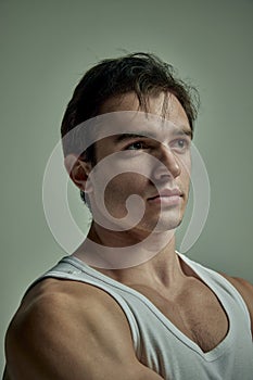 Portrait of serious handsome young man with muscular body posing in singlet over pale green studio background