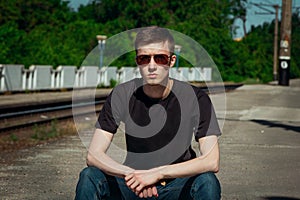 Portrait serious handsome young man sitting on a step at railway station