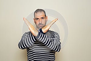 Portrait of serious Hispanic man with hands crossed, showing x sign which means stop, warning of trouble. Isolated on