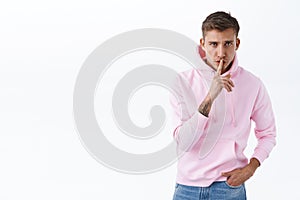 Portrait of serious-looking blond man asking politely be quiet, scolding for being noisy, shushing with finger pressed