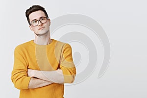 Portrait of serious-looking handsome and smart young man in glasses and yellow sweater looking with disbelief and