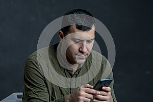 Portrait of a serious man 30-35 years old, typing in a smartphone or reading messages on a black background.