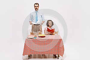 Portrait of serious man with coffee pot and tender woman reading book. Family having breakfast isolated on white