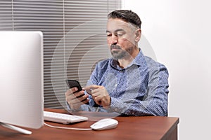 Portrait Of A Serious Mature Man Using Desktop Computer And Smart Phone